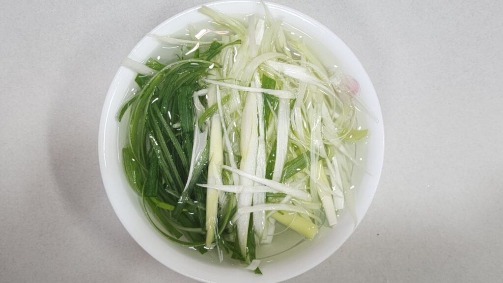 Soaking shredded scallions in a bowl of cold water to reduce sharpness