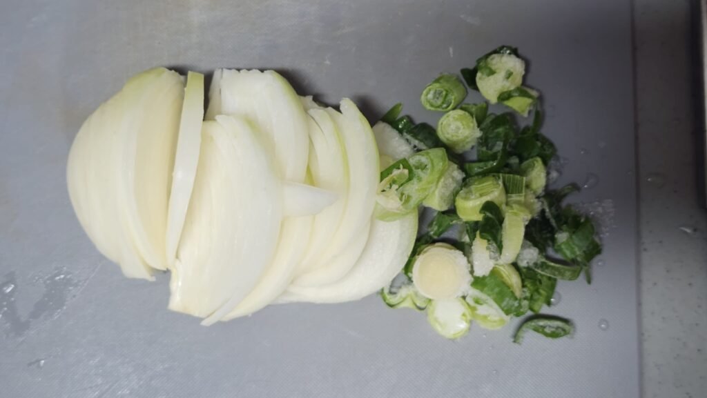 Adding sliced yellow onion and chopped white scallion to boiling water