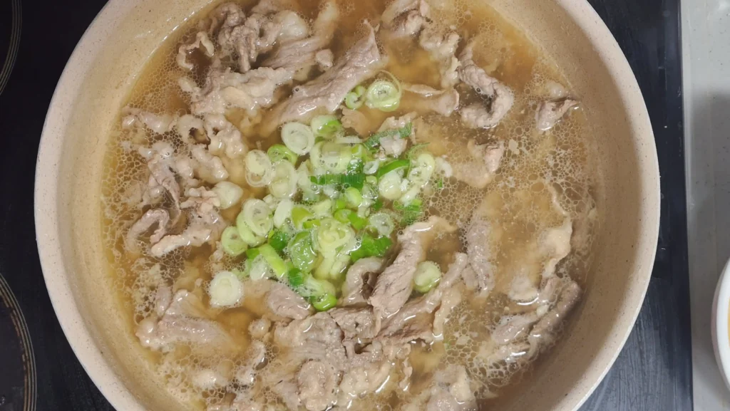 Adding thinly sliced fresh green onions to the simmering Korean beef broth