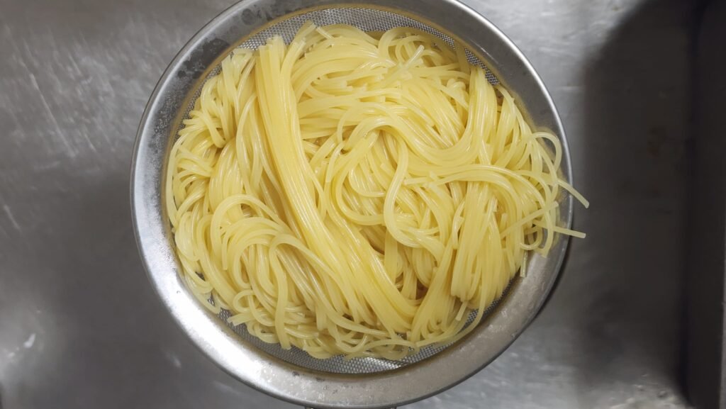 Boiled capellini noodles drained and spread out in a wide bowl to air-cool without rinsing in cold water
