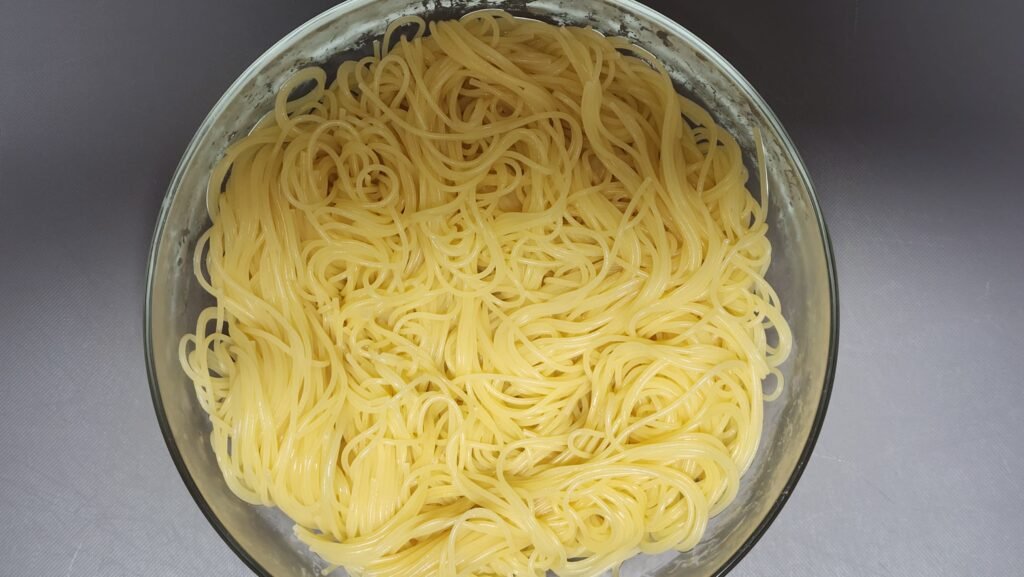 Boiled capellini noodles drained and spread out in a wide bowl to air-cool without rinsing in cold water