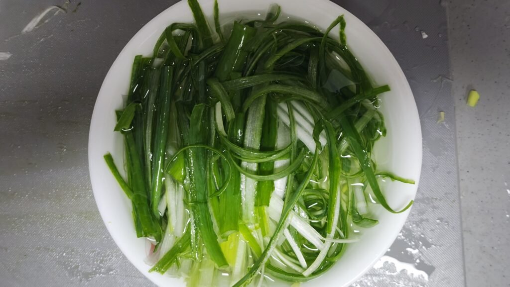 Thinly shredded green onions soaking in a bowl of cold water to remove harshness, then dried on paper towels
