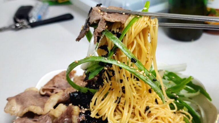 Close-up of cold perilla oil pasta garnished with shredded green onions, crushed seasoned seaweed snack, and toasted sesame seeds