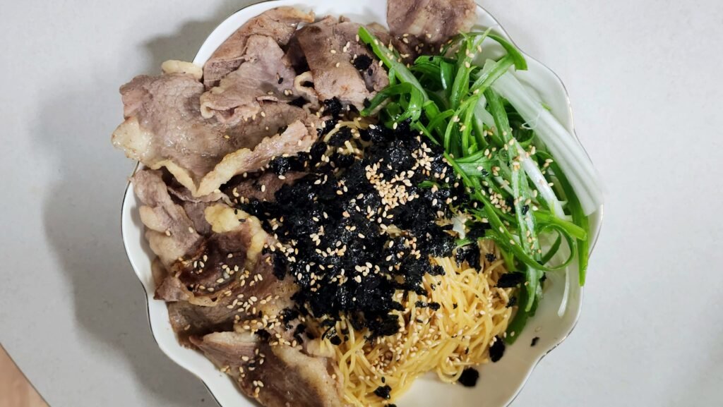 Close-up of cold perilla oil pasta garnished with shredded green onions, crushed seasoned seaweed snack, and toasted sesame seeds
