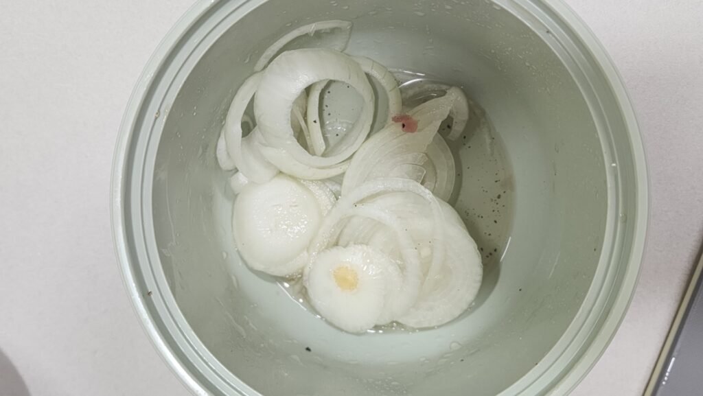 Placing marinated pork belly on a bed of sliced yellow onions before microwaving