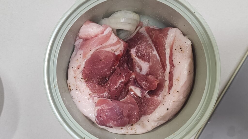 Placing marinated pork belly on a bed of sliced yellow onions before microwaving