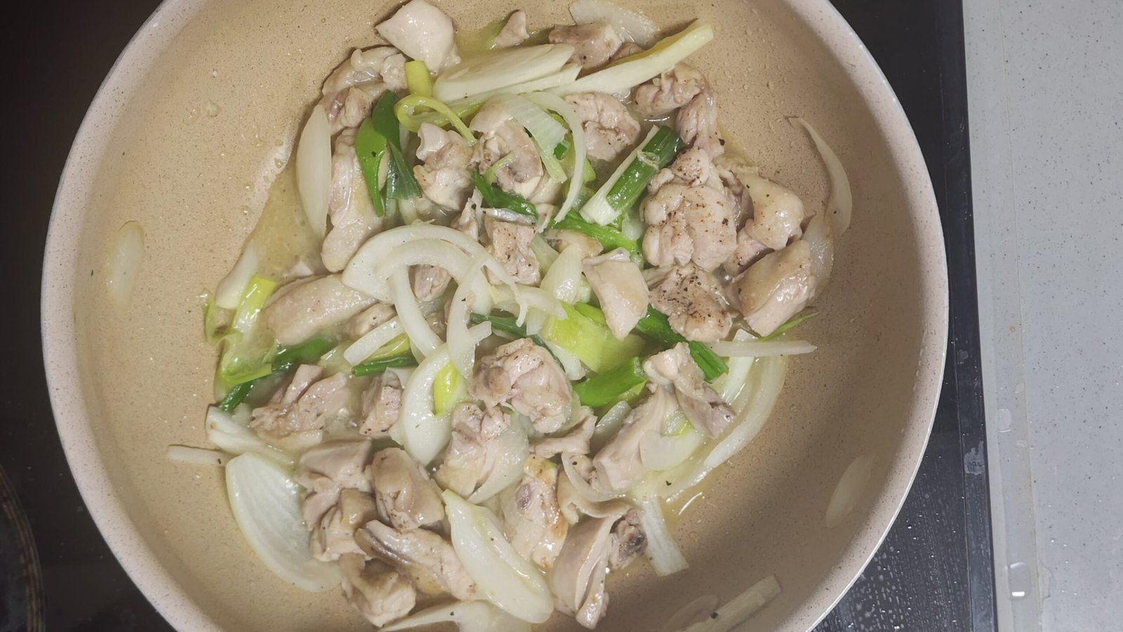 Adding sliced onion, Korean green onion, and minced garlic to the pan with the chicken.