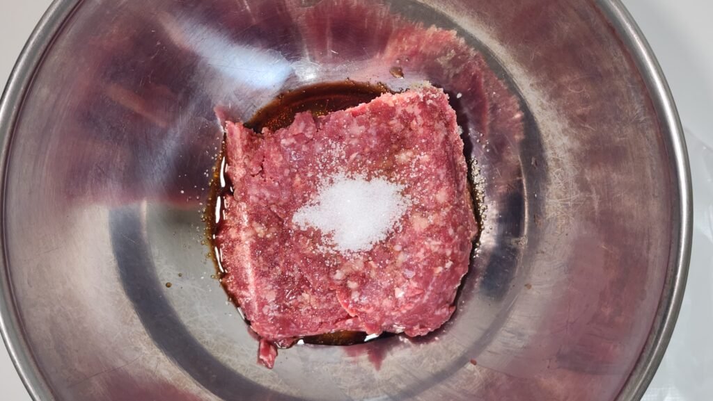 Ground beef with soy sauce, mirin, sugar, and minced garlic in a bowl.