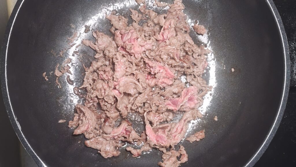 Briefly cooking thinly sliced beef in oil over medium heat before adding the vegetables.