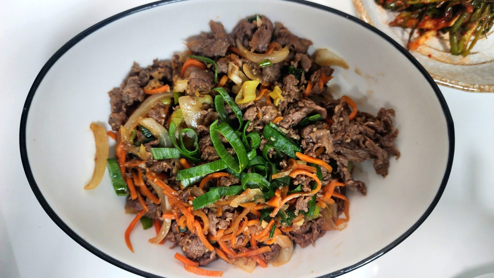 Cooking the beef and vegetables in the sauce until the beef is fully cooked, then finishing with a drizzle of sesame oil.