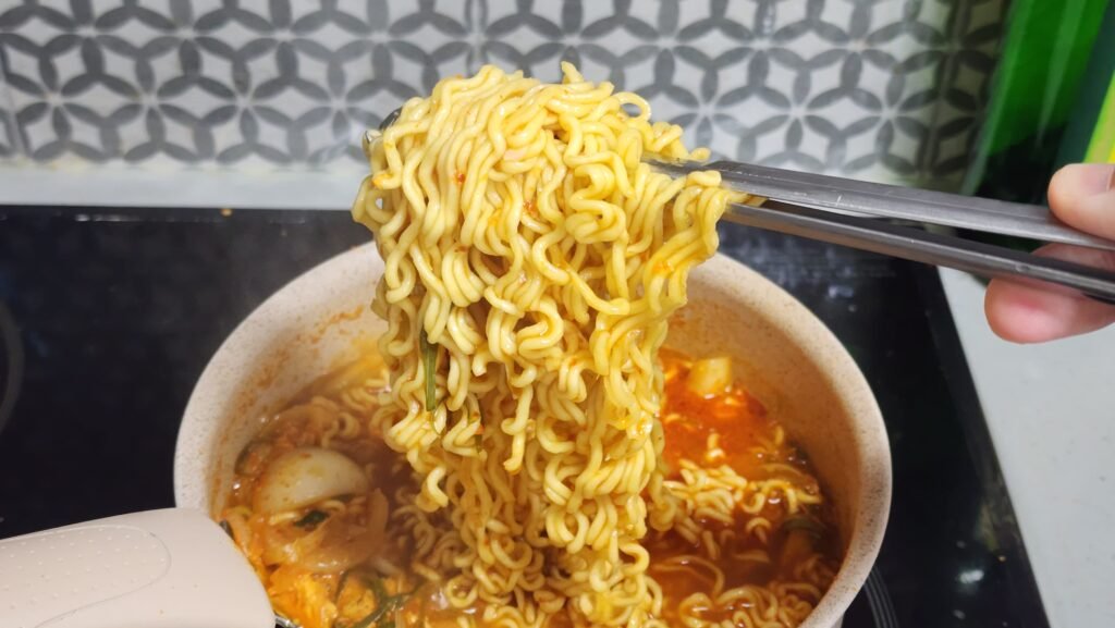 Lifting the noodles out of the broth with tongs while they cook.