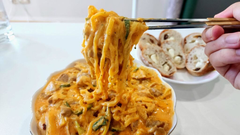 Finished Rosé Buldak jjimdak with chicken thigh, ramen, onion, and Korean green onion in a creamy milk and cheddar sauce.