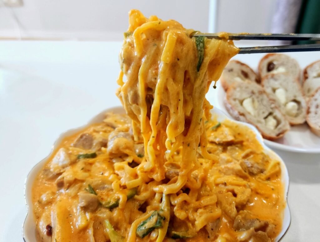 Finished Rosé Buldak jjimdak with chicken thigh, ramen, onion, and Korean green onion in a creamy milk and cheddar sauce.