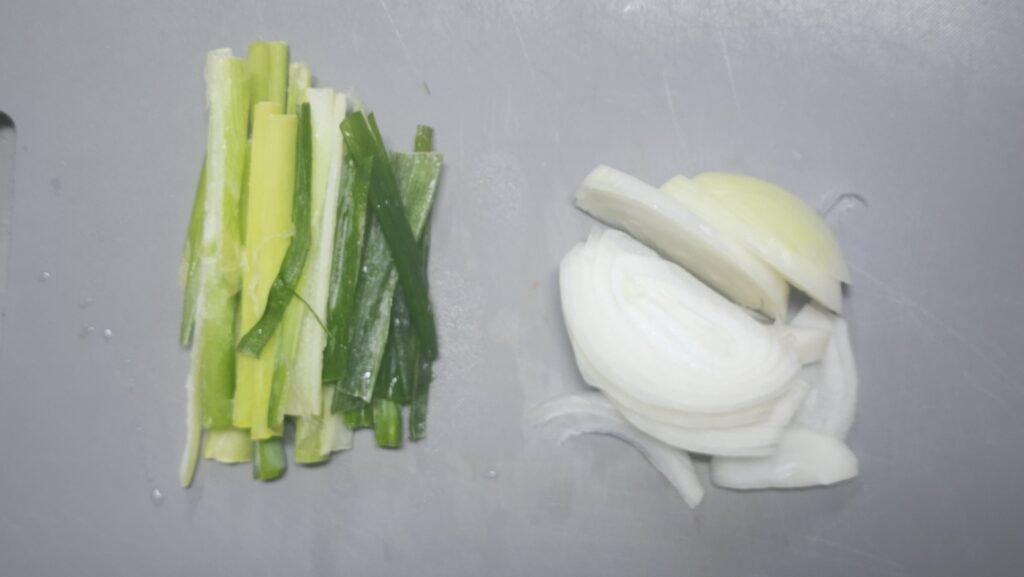 Thinly slicing the onion and cutting Korean green onion into bite-sized pieces for Rosé Buldak jjimdak.