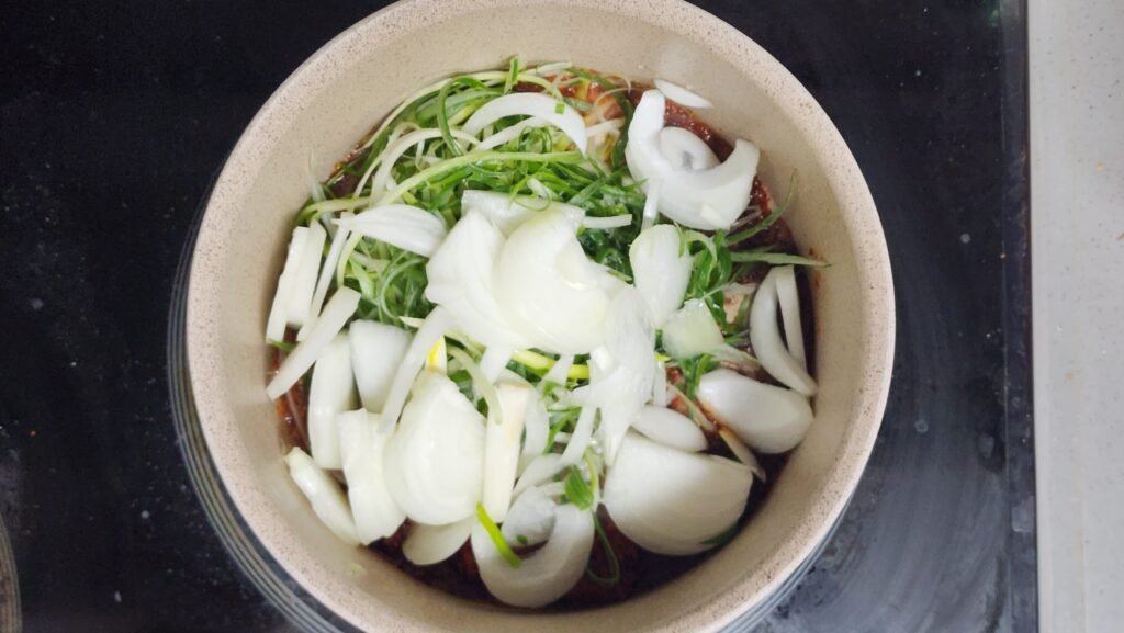 Stir-frying garlic, gochugaru, green onion, and onion in heated olive oil for about 2 minutes.