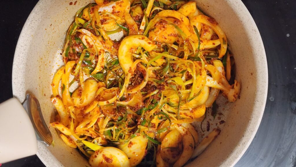 Stir-frying garlic, gochugaru, green onion, and onion in heated olive oil for about 2 minutes.