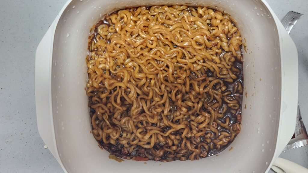 Mixing Chapagetti black bean sauce powder with noodles and water in a microwave bowl