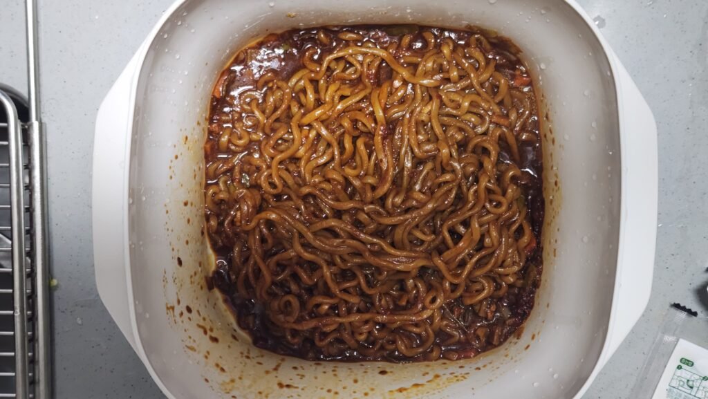 Pouring fresh chili oil over cooked Chapagetti noodles before the final 30-second heat