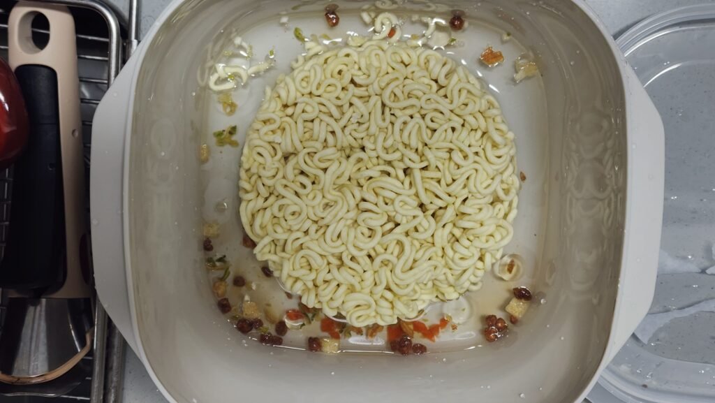 Chapagetti noodles in a microwave-safe bowl with water and seasoning oil before cooking